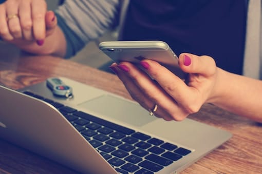 a woman using a cell phone while sitting in front of a laptop.