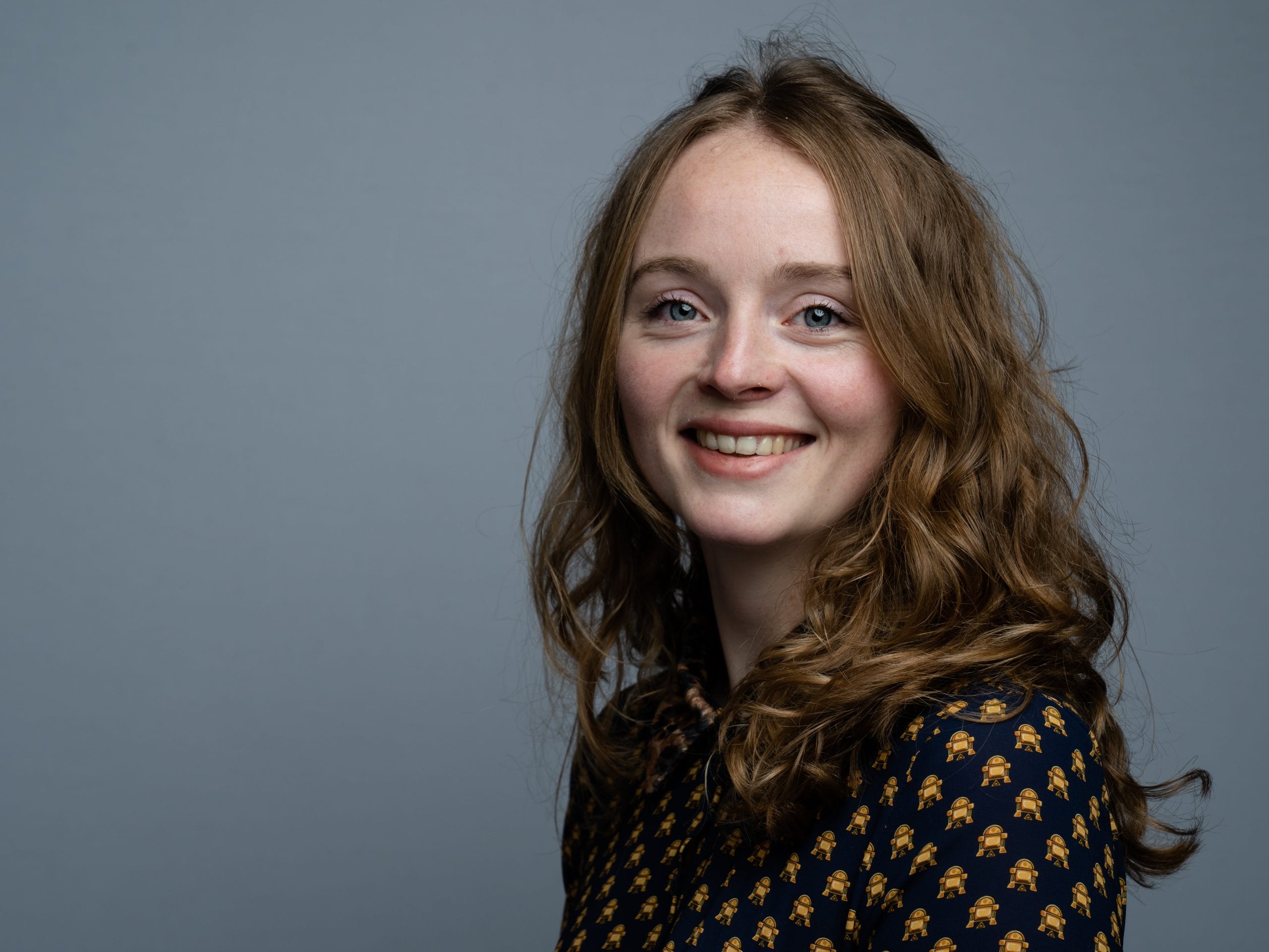 Portrait d'une femme souriante aux cheveux bouclés sur fond gris. Portrait of a smiling woman with curly hair against a grey background.